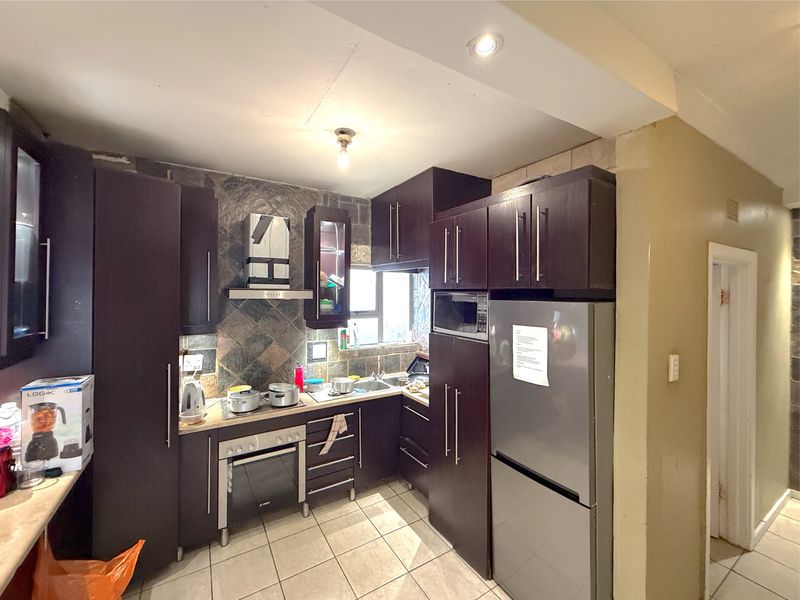 A compact kitchen featuring dark wood cabinetry, a built-in oven, extractor fan, and tiled backsplash with neutral floor tiles.