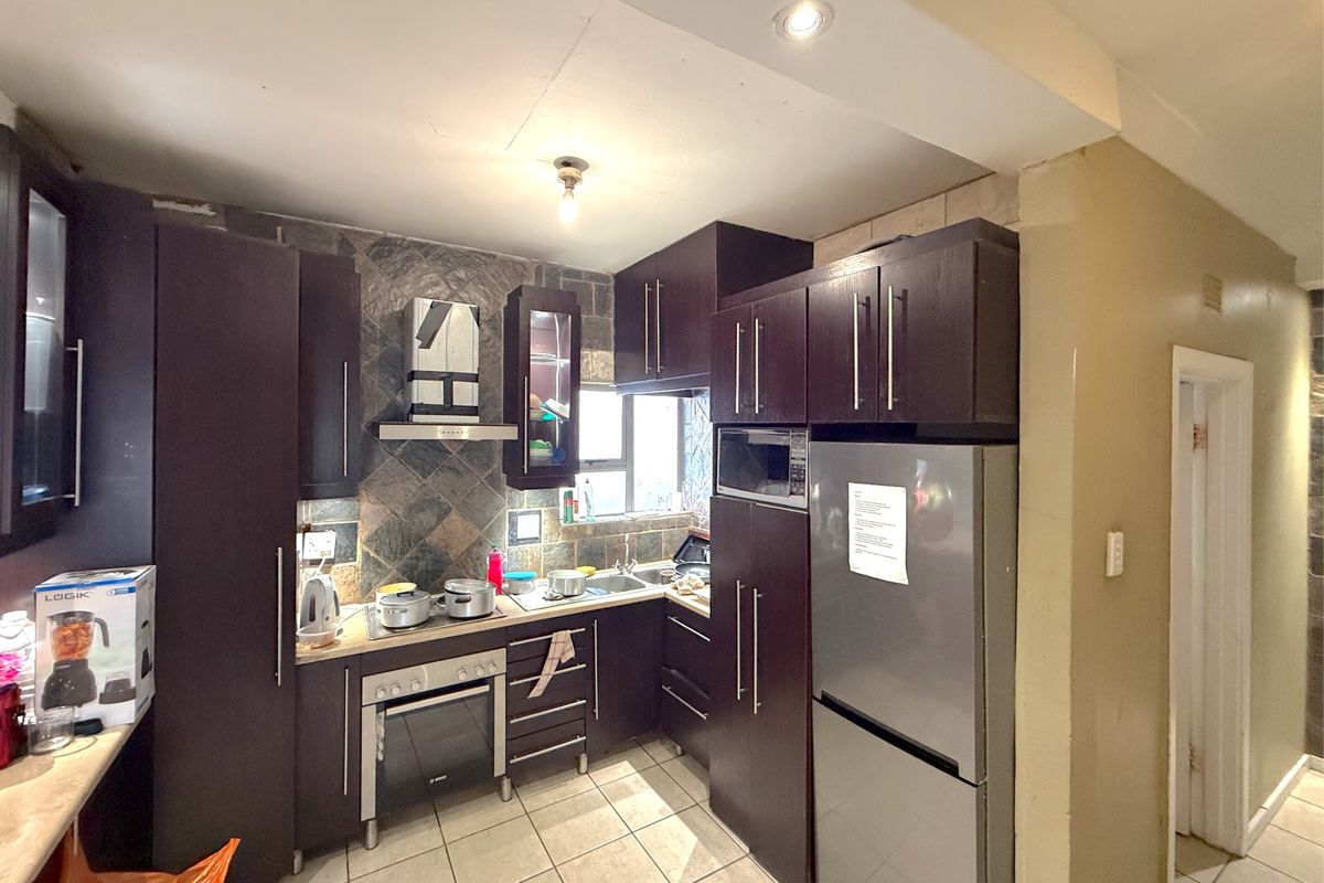 A compact kitchen featuring dark wood cabinetry, a built-in oven, extractor fan, and tiled backsplash with neutral floor tiles.