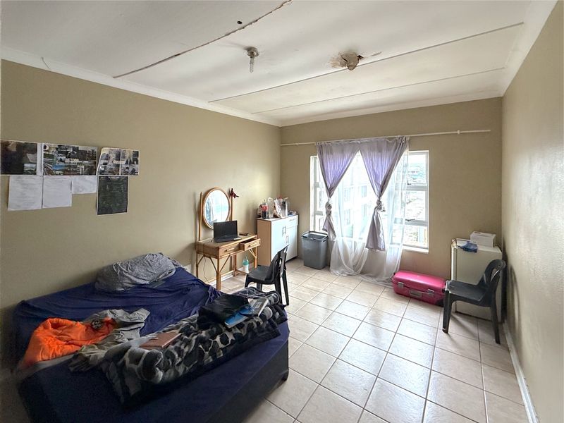 A bedroom featuring tiled flooring and a window, currently showing visible signs of ceiling damage and cracking requiring maintenance.