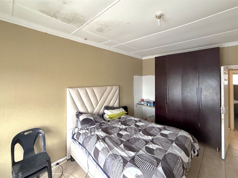 A bedroom featuring tiled flooring and a built-in wardrobe, currently showing signs of ceiling water damage and unfinished wall paint requiring maintenance.