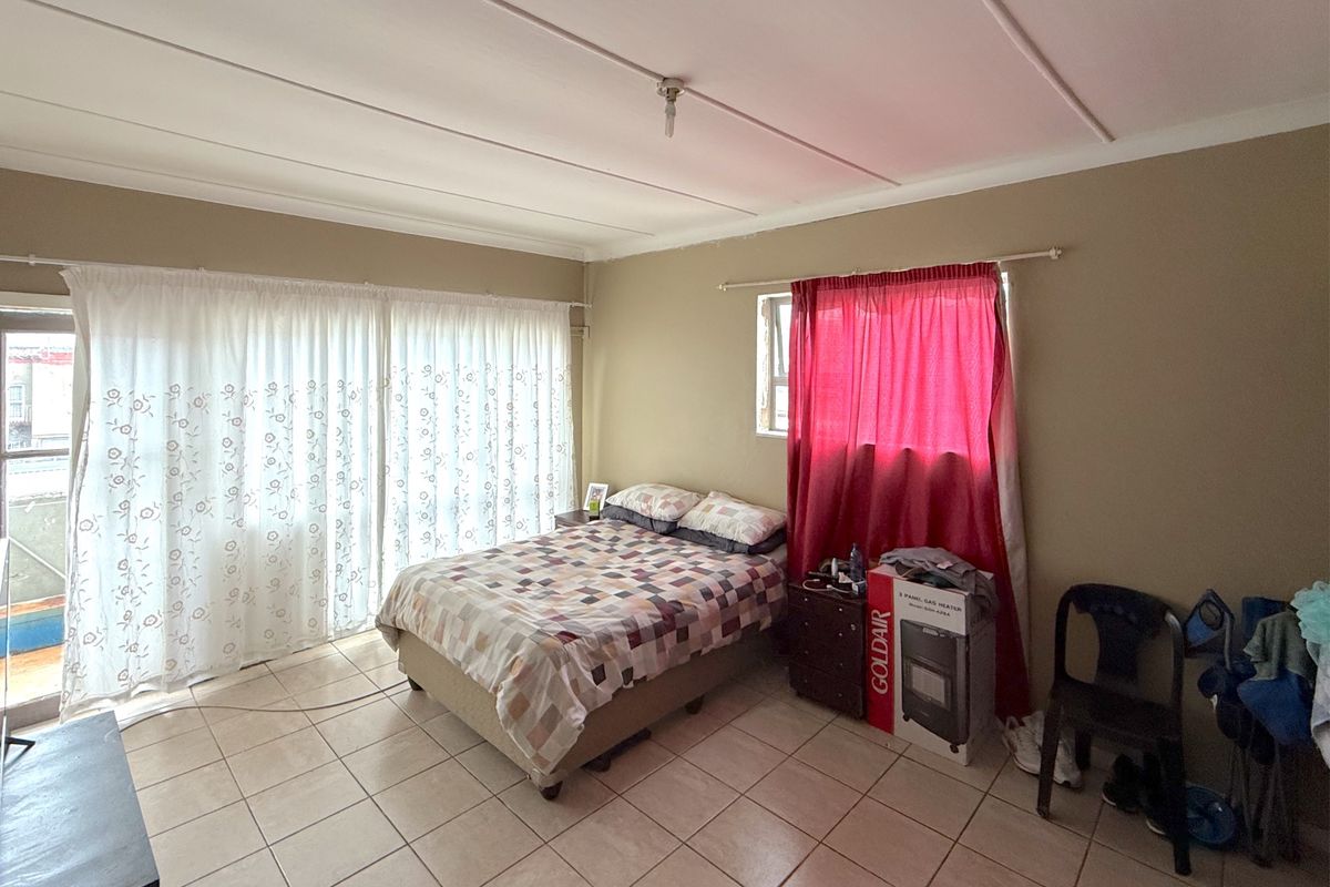 A bedroom featuring tiled flooring, a sliding glass door providing natural light, and a window with curtains.
