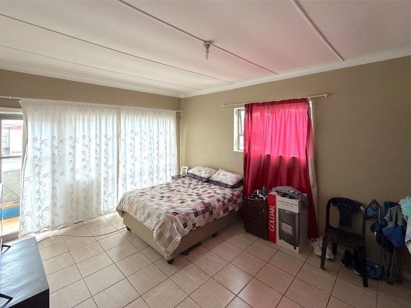 A bedroom featuring tiled flooring, a sliding glass door providing natural light, and a window with curtains.