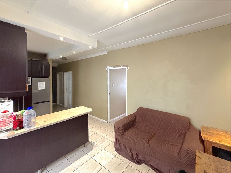Open plan living area featuring tiled flooring, a breakfast bar, and kitchen cabinetry, requiring minor repairs to door frames and wall finishes.