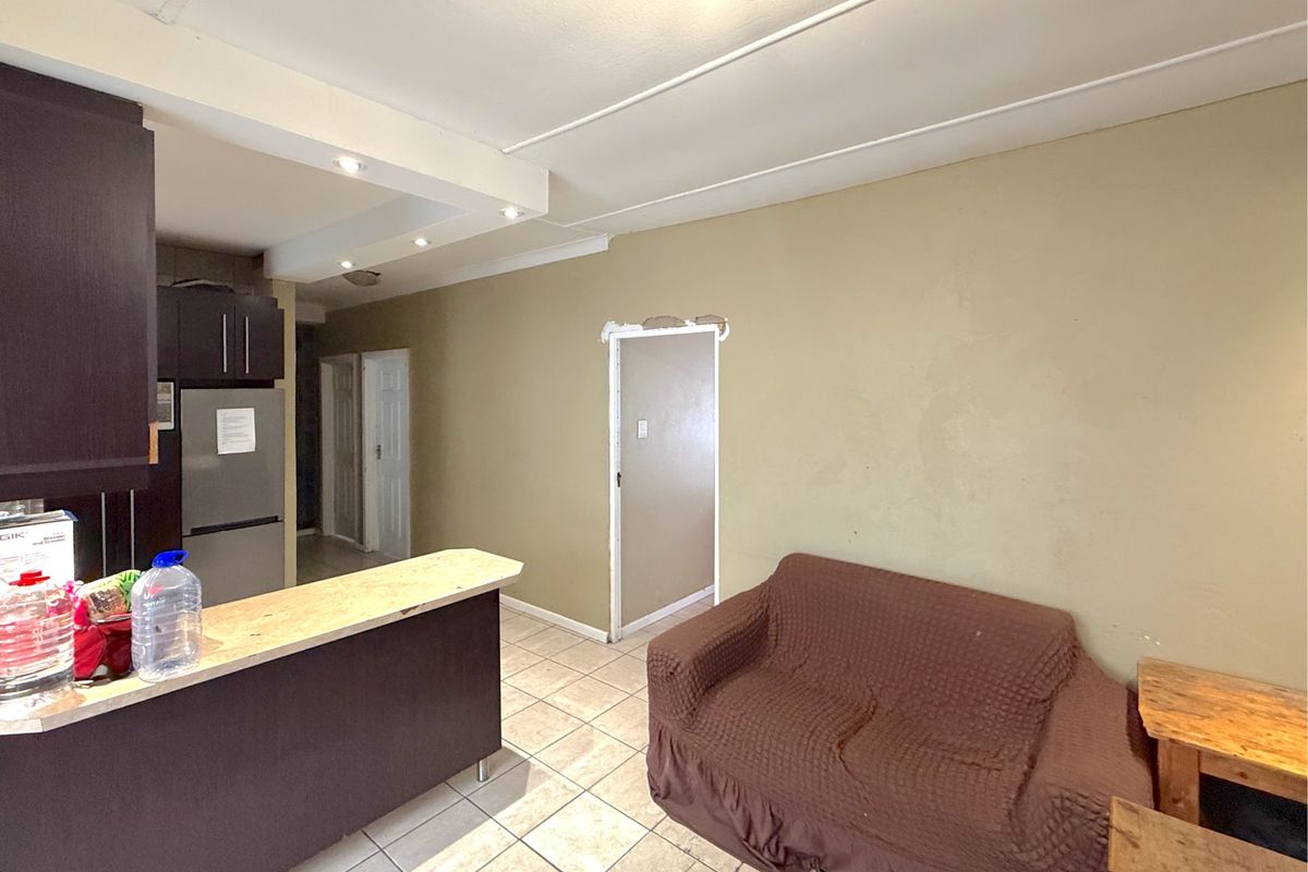 Open plan living area featuring tiled flooring, a breakfast bar, and kitchen cabinetry, requiring minor repairs to door frames and wall finishes.