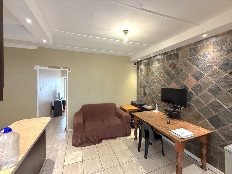 Living area featuring a stone accent wall, tiled flooring, and recessed ceiling lighting, with some minor cosmetic repairs needed around the doorway.