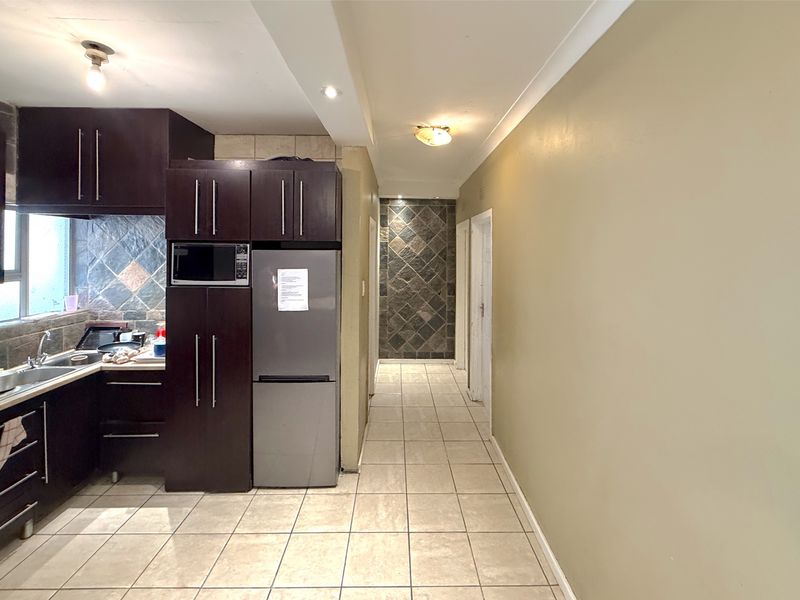 A functional kitchen area featuring dark cabinetry, tiled backsplash, and a stone feature wall, leading into a tiled hallway.