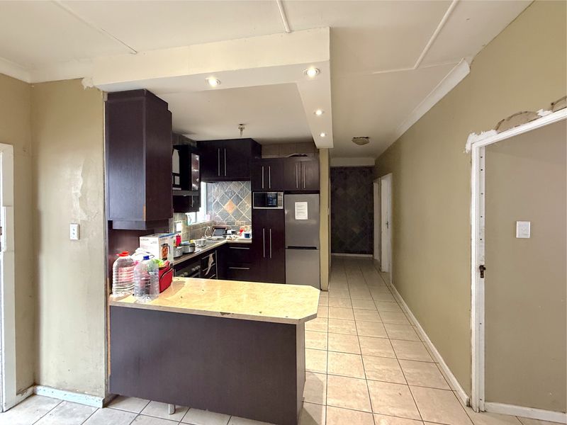 A compact kitchen featuring dark cabinetry, stone countertops, and tiled flooring, requiring cosmetic updates to the wall finishes and general maintenance.