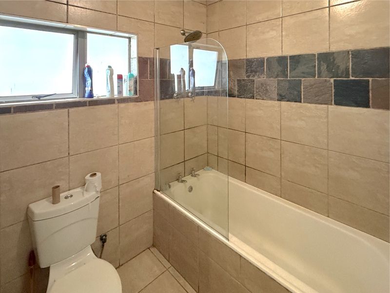 A functional bathroom featuring a bathtub with a glass shower screen, tiled walls with decorative accents, and a standard toilet.