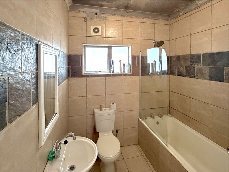 A dated bathroom featuring a bathtub with a glass screen, pedestal basin, and toilet, requiring renovation to address ceiling and tile condition.