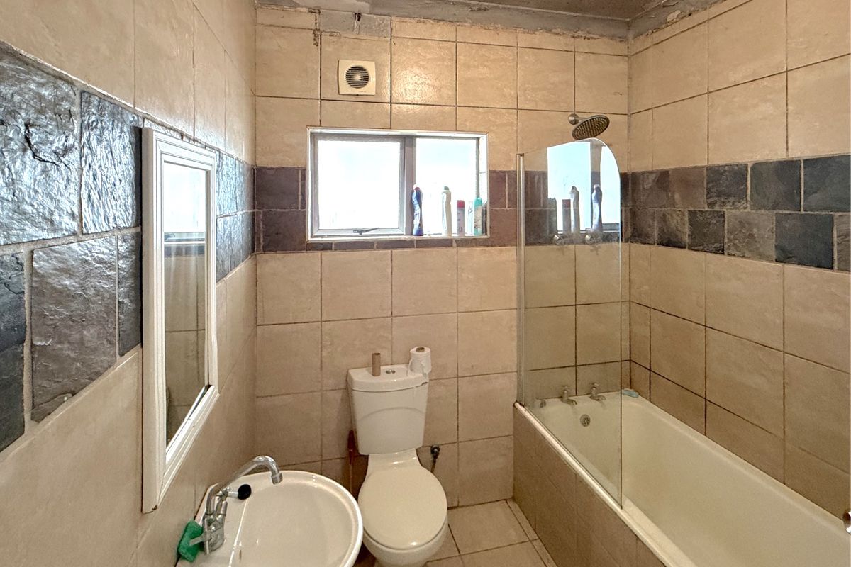 A dated bathroom featuring a bathtub with a glass screen, pedestal basin, and toilet, requiring renovation to address ceiling and tile condition.