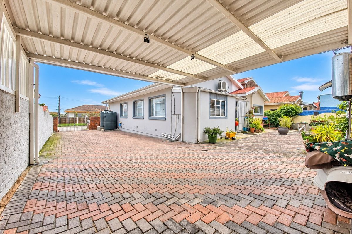 A spacious paved rear courtyard featuring a large covered carport, water storage tank, and exterior wall-mounted air conditioning unit.
