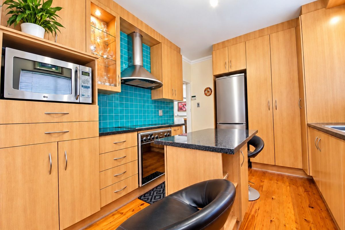 A well-maintained kitchen featuring timber cabinetry, granite countertops, a vibrant tiled splashback, and integrated stainless steel appliances.