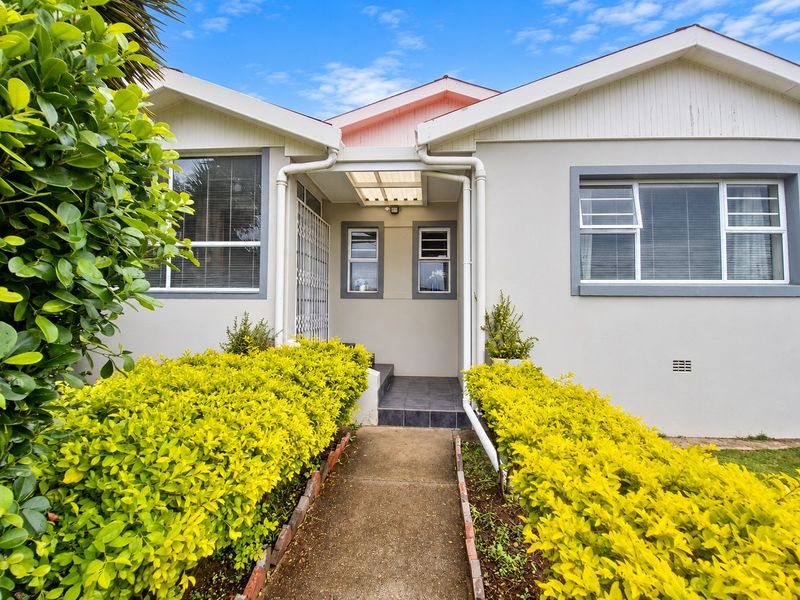 Front entrance of the house featuring a concrete walkway, landscaped garden borders, and a covered porch area with tiled flooring.