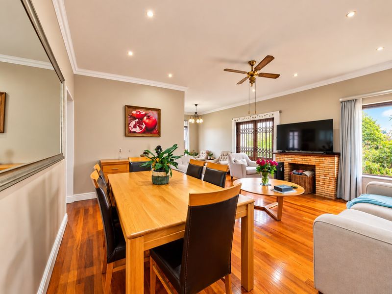 Spacious open-plan living and dining area featuring polished hardwood floors, a brick fireplace, and abundant natural light through sliding glass doors.