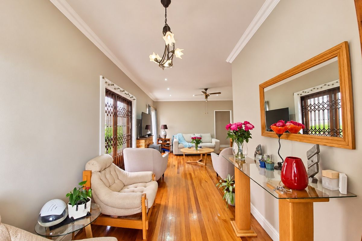 A well-maintained living room featuring polished hardwood flooring, crown molding, and a ceiling fan, with natural light entering through a secure sliding door.
