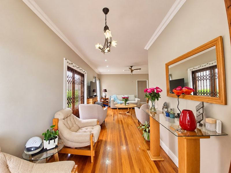 A well-maintained living room featuring polished hardwood flooring, crown molding, and a ceiling fan, with natural light entering through a secure sliding door.