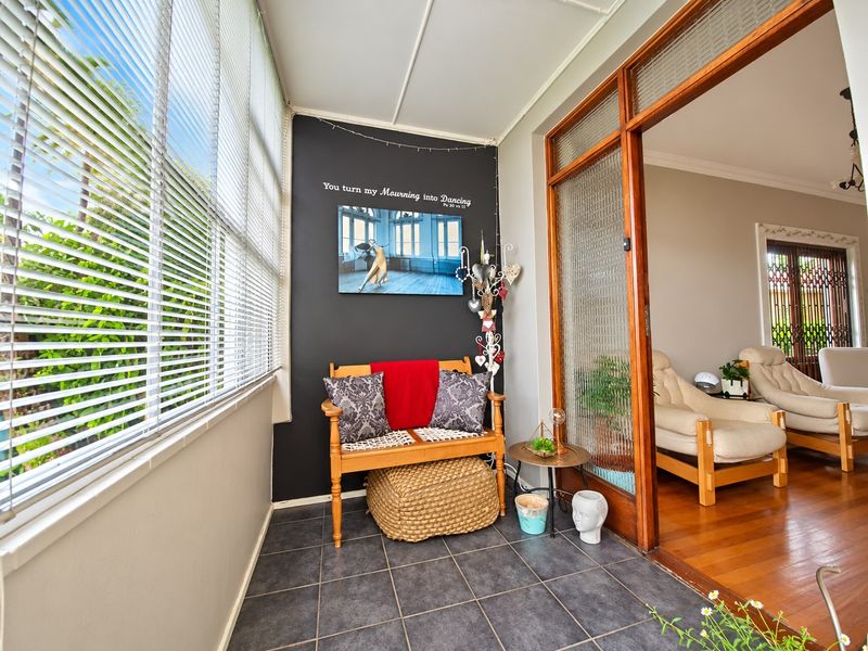 A bright, enclosed patio area featuring dark tiled flooring, large windows with venetian blinds, and a timber-framed sliding door leading to the living space.