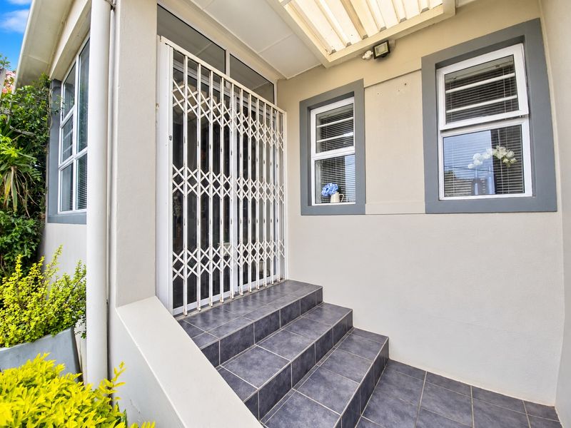 A well-maintained entrance featuring tiled steps, a secure metal gate, and aluminium-framed windows under a covered porch area.