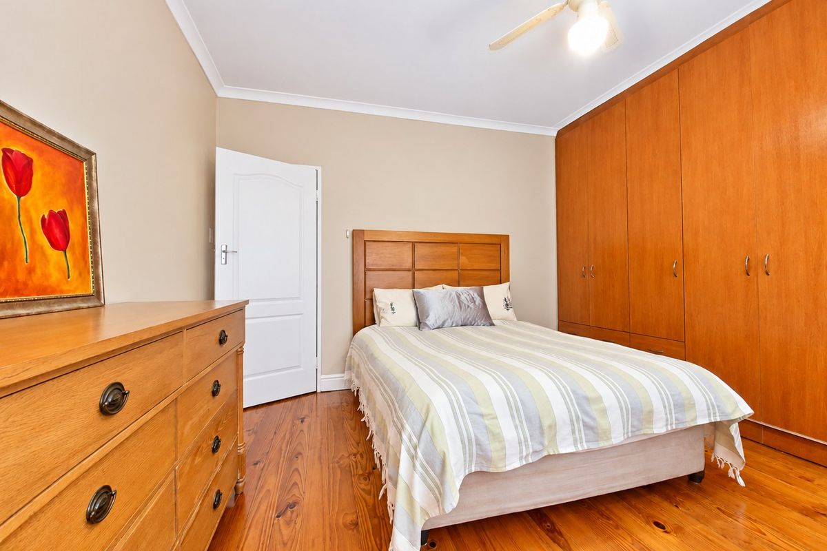 A well-maintained bedroom featuring warm timber flooring, extensive built-in wooden cupboards, and a functional ceiling fan.