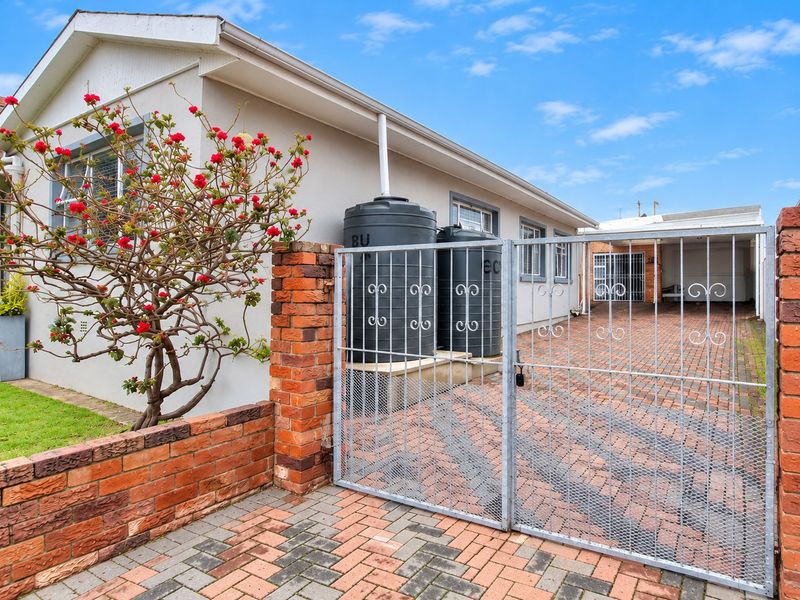 Front exterior view featuring a paved driveway, secure metal gate, brick boundary wall, and installed water storage tanks alongside the house structure.