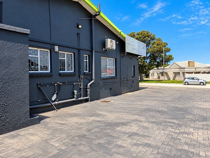 Exterior view of the property featuring a paved driveway, dark painted facade, security bars on windows, and external utility installations.