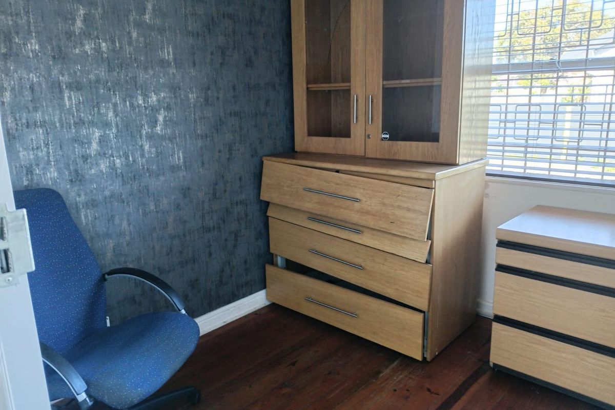 A bedroom featuring timber flooring, a textured feature wall, and window security bars.