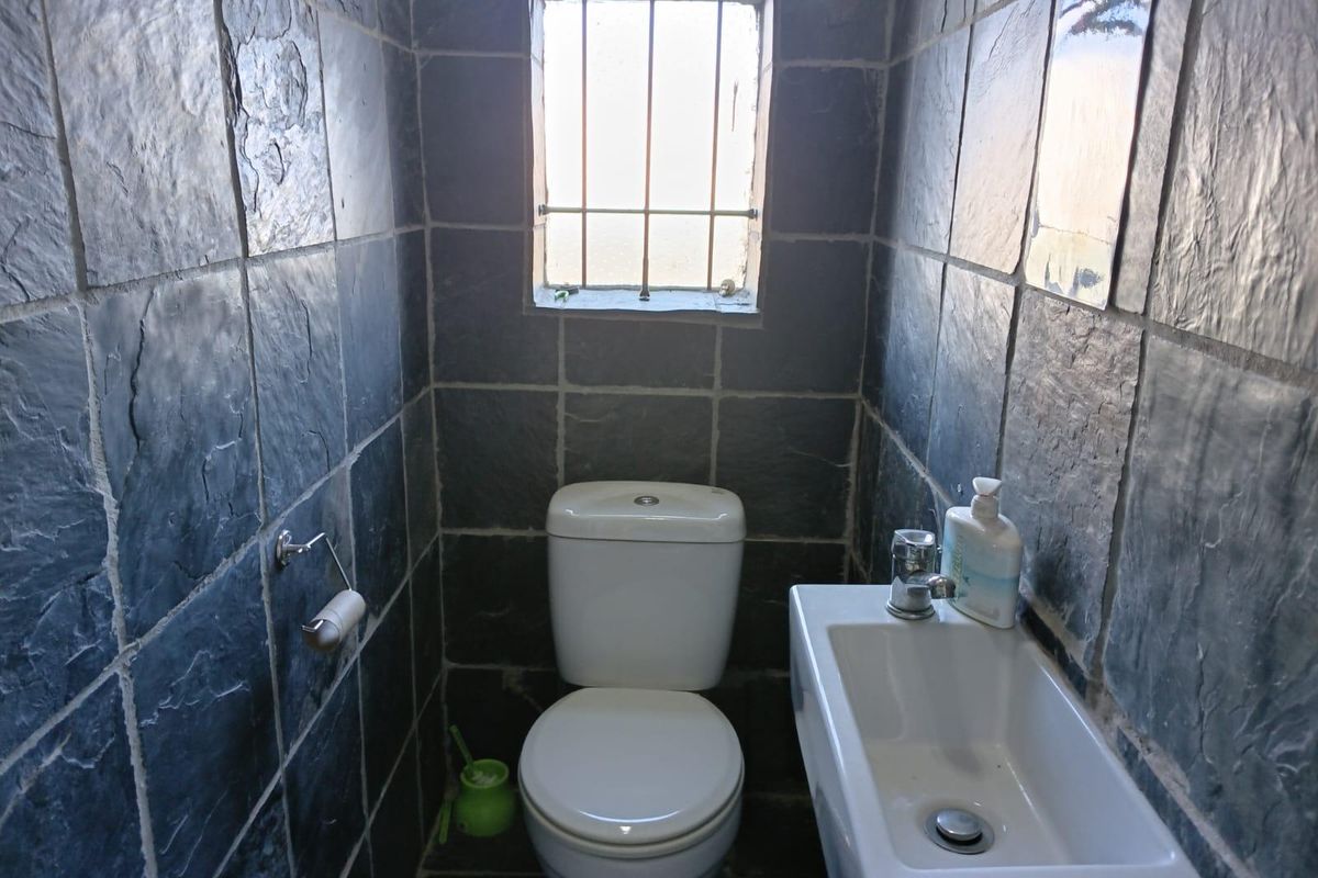 A compact guest bathroom featuring dark slate wall and floor tiles, a white toilet, and a small wall-mounted basin.