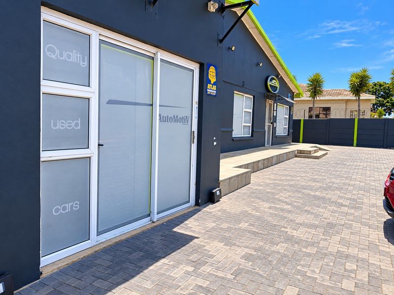 Front exterior view of a commercial-style property featuring a paved driveway, sliding glass entrance doors, and a secure perimeter wall.