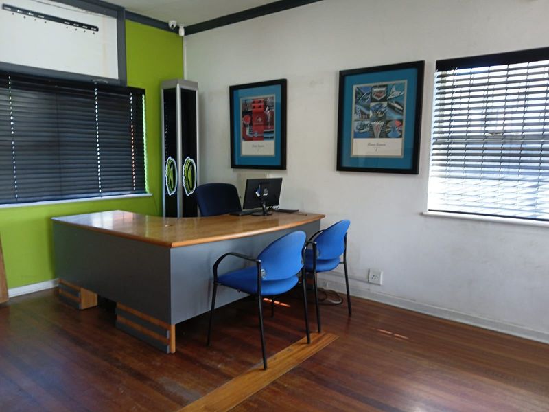 A functional home office space featuring hardwood flooring, large windows with venetian blinds, and a vibrant accent wall.
