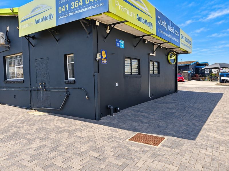 Exterior view of a commercial property featuring a paved driveway, dark painted facade, and security-fitted windows.
