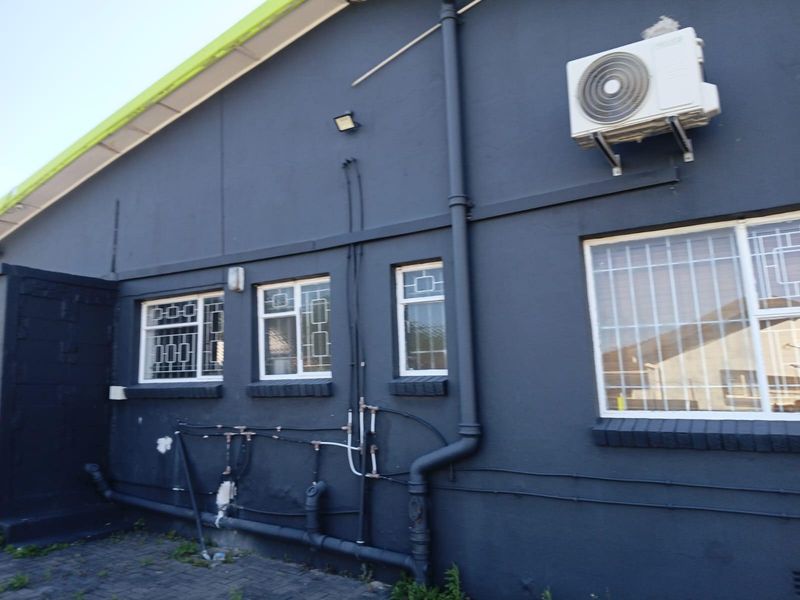 Rear exterior view of the property featuring dark painted walls, security-barred windows, and external plumbing infrastructure.