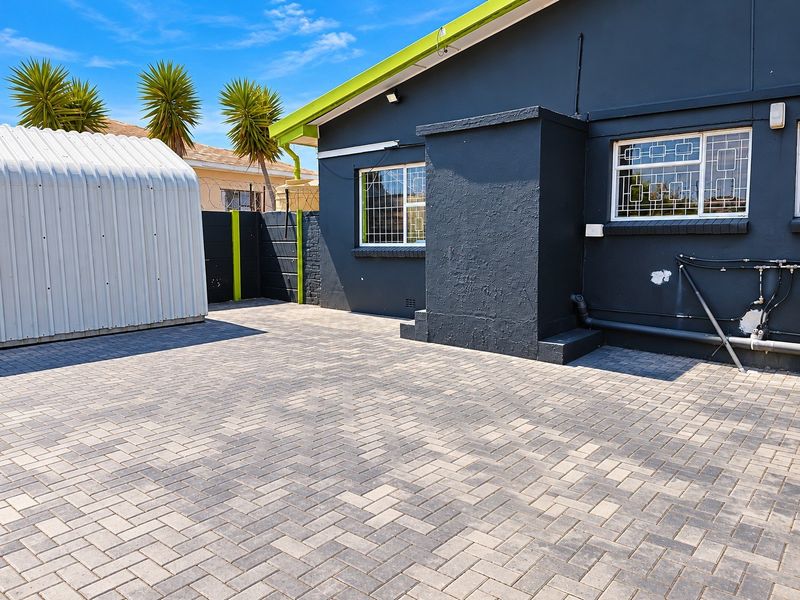Rear exterior area featuring paved surfacing, a metal storage shed, and a dark-painted building facade with security-barred windows.