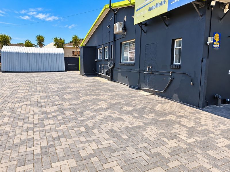 Rear exterior view of the property featuring a large paved driveway, a metal storage shed, and external building infrastructure.