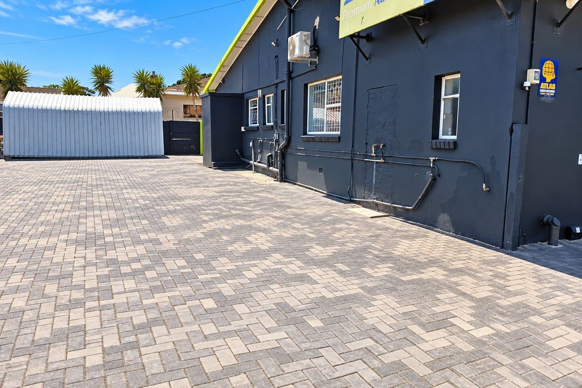 Rear exterior view of the property featuring a large paved driveway, a metal storage shed, and external building infrastructure.