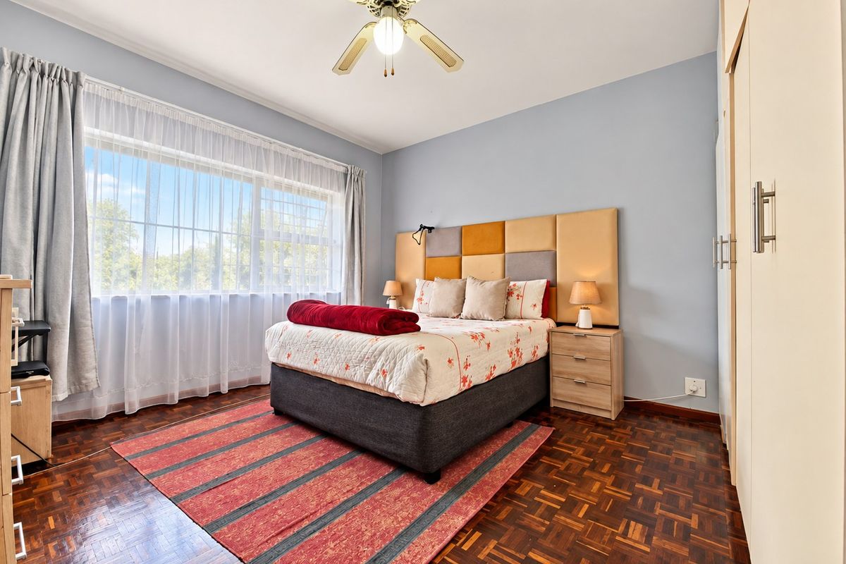 A well-maintained bedroom featuring classic parquet flooring, built-in storage cupboards, and a ceiling fan, offering a comfortable and functional living space.