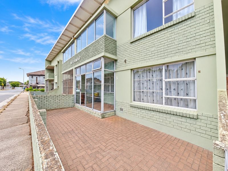 Front elevation of the Miramar apartment building featuring a paved patio area, brick facade, and enclosed entrance porch with aluminium window frames.