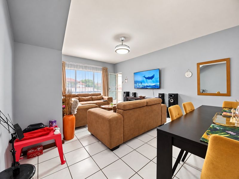 Open-plan living and dining area featuring tiled flooring, a ceiling fan, and large windows providing natural light and access to the balcony.