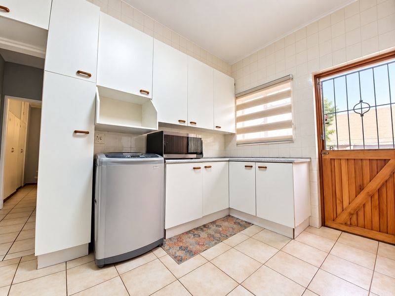 A functional laundry area featuring white built-in cabinetry, tiled flooring, and a timber exterior door with a security gate.