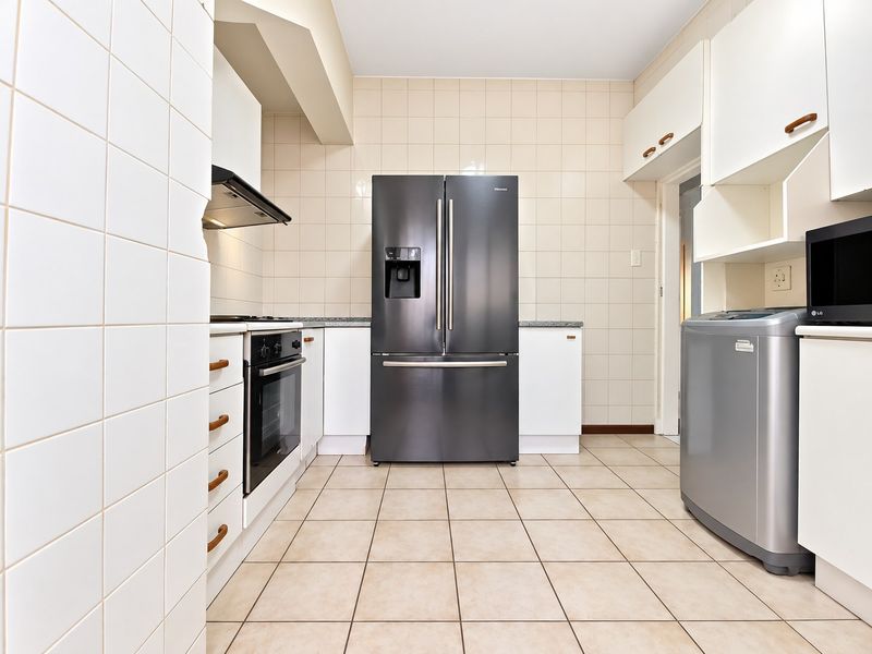 A functional kitchen featuring tiled walls and flooring, built-in cabinetry, a modern oven, and an extractor fan, providing a clean and practical workspace.