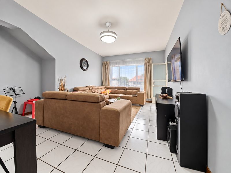 A bright and spacious living room featuring neutral tiled flooring, a central ceiling fan, and large windows that provide ample natural light.