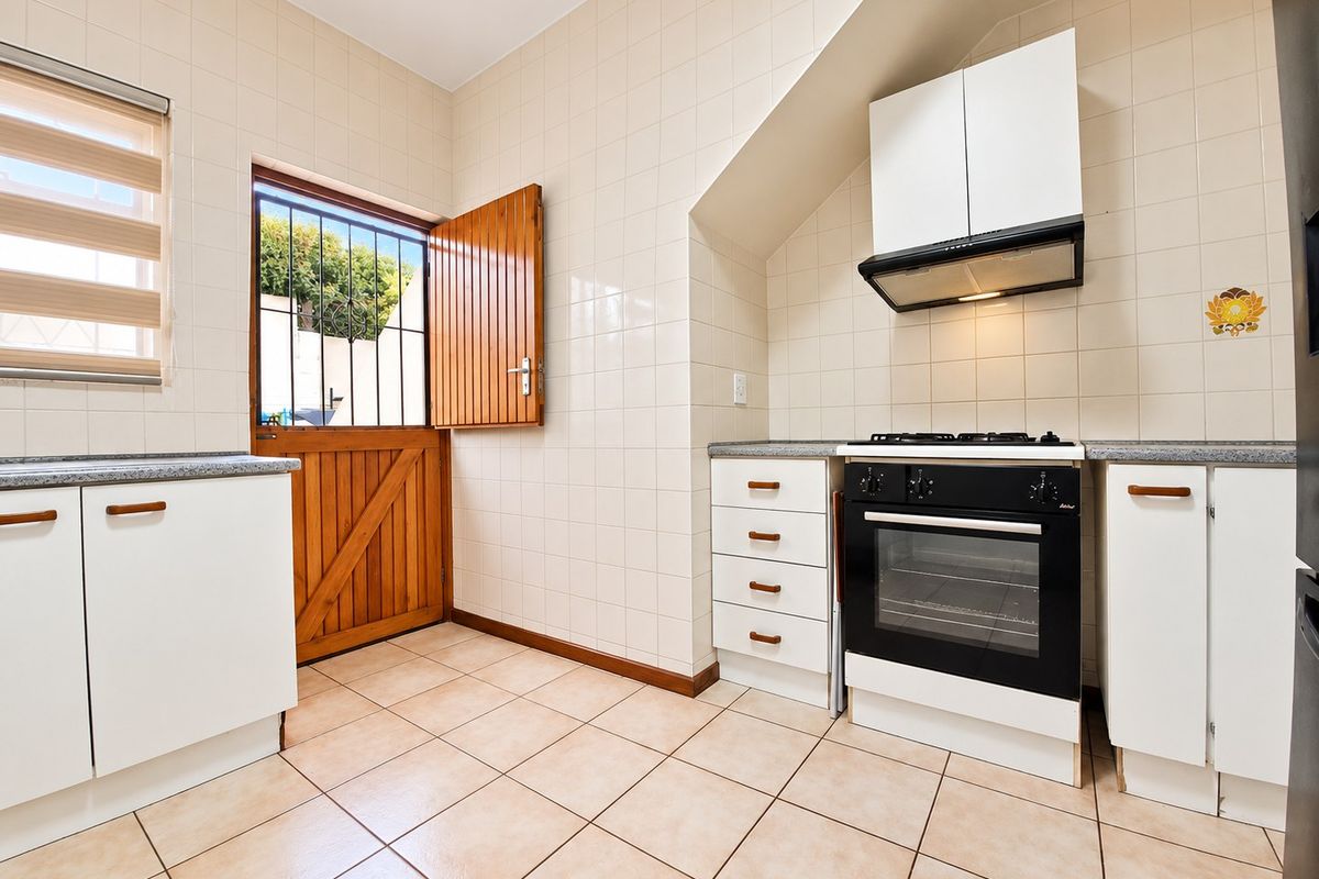 A functional kitchen featuring tiled walls and floors, built-in cabinetry, a gas stove with oven, and a stable door leading to the exterior.
