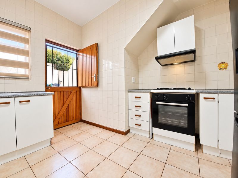 A functional kitchen featuring tiled walls and floors, built-in cabinetry, a gas stove with oven, and a stable door leading to the exterior.