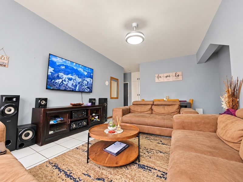 A well-maintained living room featuring tiled flooring, a ceiling fan, and built-in storage cupboards, offering a comfortable and functional living space.