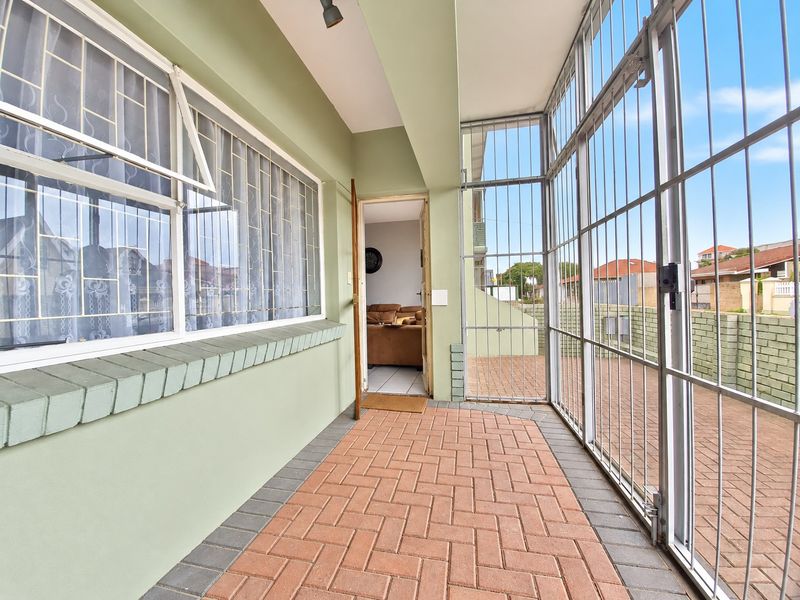 A covered patio area featuring brick paving, secure metal security gates, and protective window bars, providing a functional outdoor transition space.