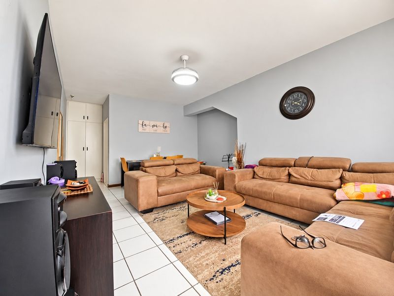 A spacious living room featuring tiled flooring, a ceiling fan, and built-in storage cupboards, offering a functional and comfortable layout.