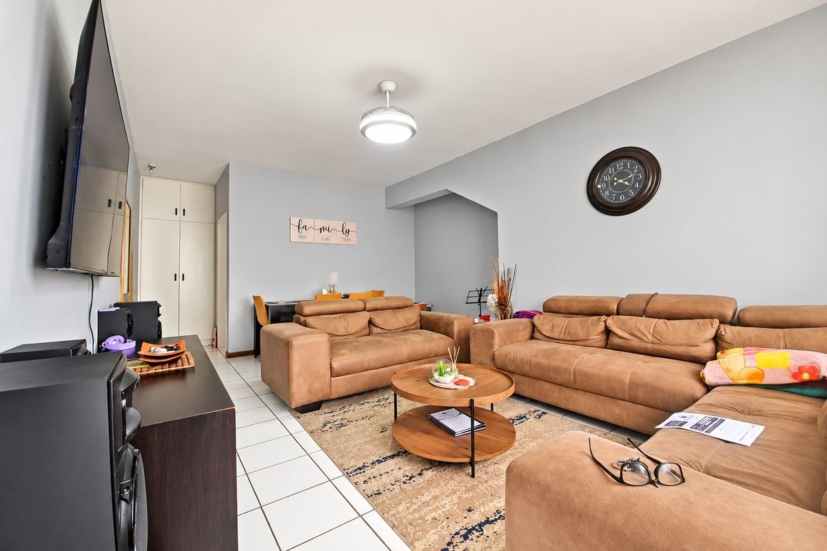 A spacious living room featuring tiled flooring, a ceiling fan, and built-in storage cupboards, offering a functional and comfortable layout.