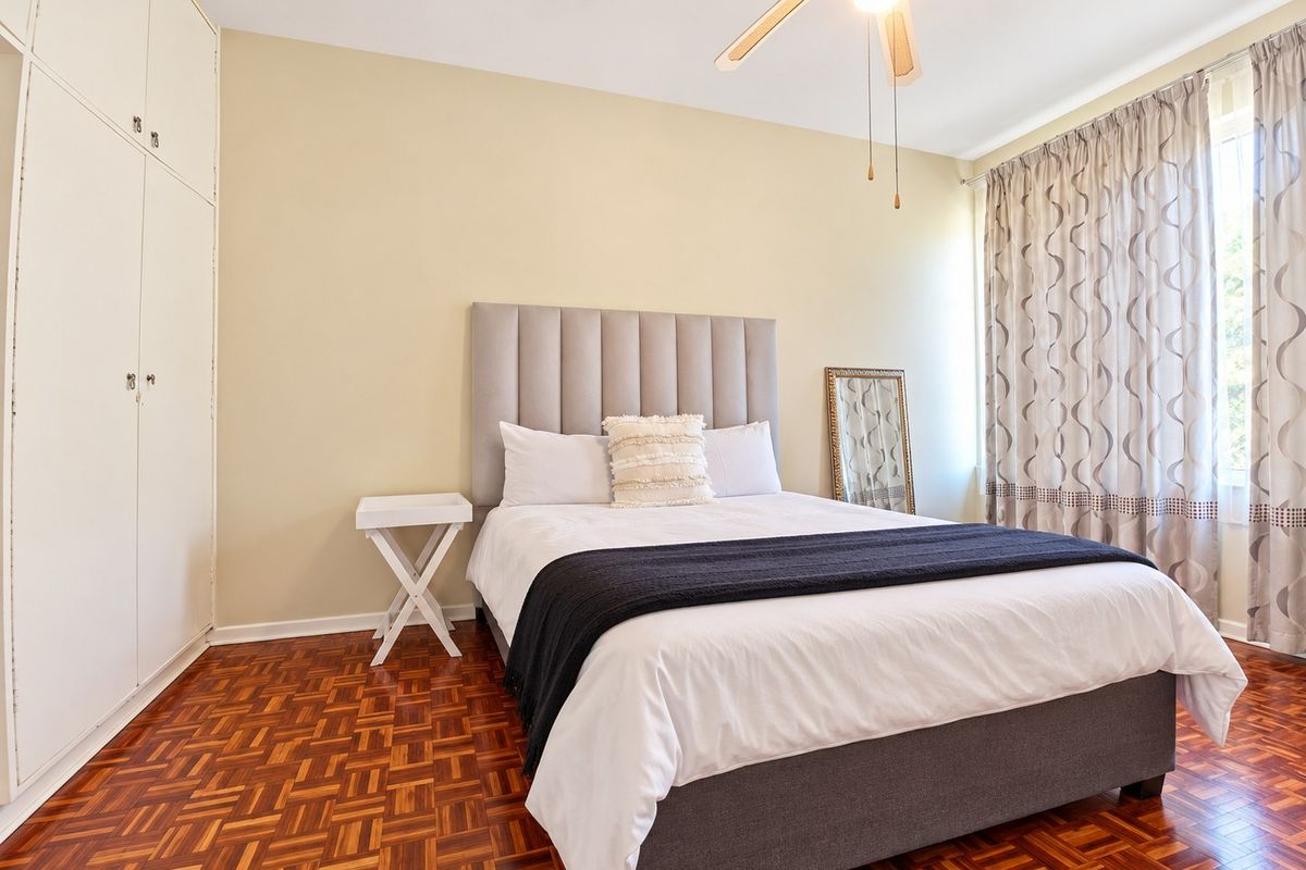 A well-maintained bedroom featuring classic parquet flooring, built-in storage cupboards, and a ceiling fan, offering a comfortable and functional living space.