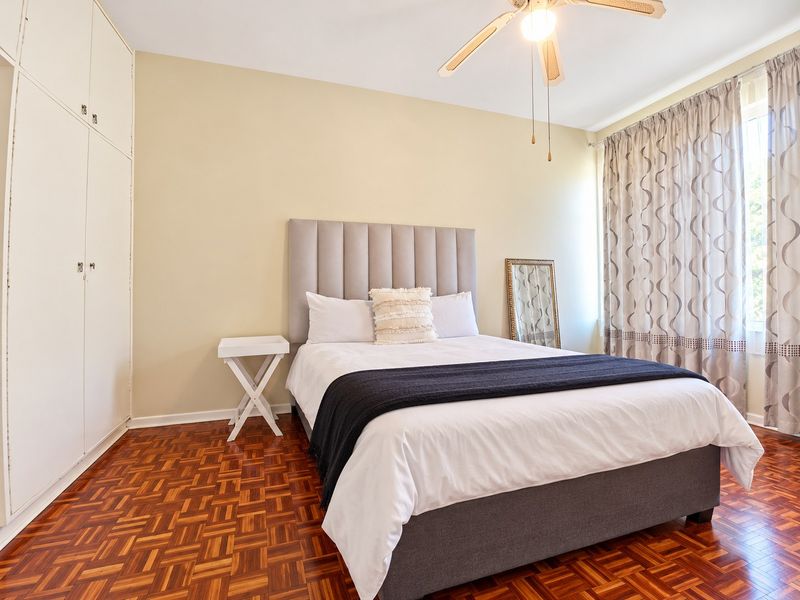 A well-maintained bedroom featuring classic parquet flooring, built-in storage cupboards, and a ceiling fan, offering a comfortable and functional living space.