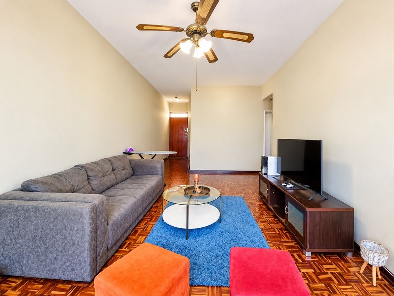 A living room featuring traditional parquet flooring, a ceiling fan, and neutral wall tones, providing a functional and well-lit space.