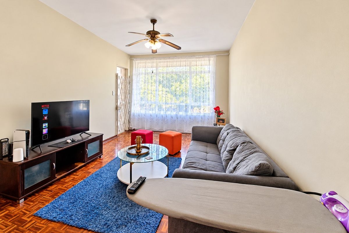 A comfortable living room featuring classic parquet flooring, a ceiling fan, and a large window that allows for natural light.